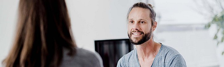 zwei menschen miteinander im Gespräch, eine Person ist nur von hinten zu sehen